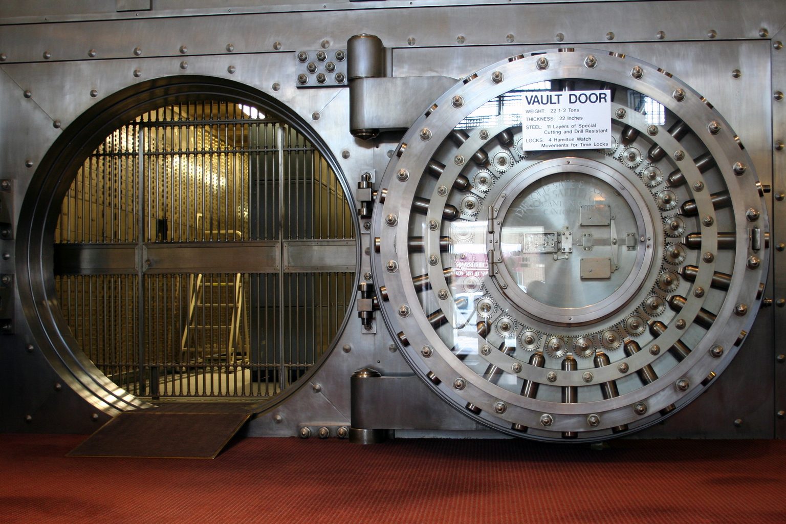 Geöffnete runde Tür eines alten Banktresors, dahinter ein Gitter vor den Schließfächern