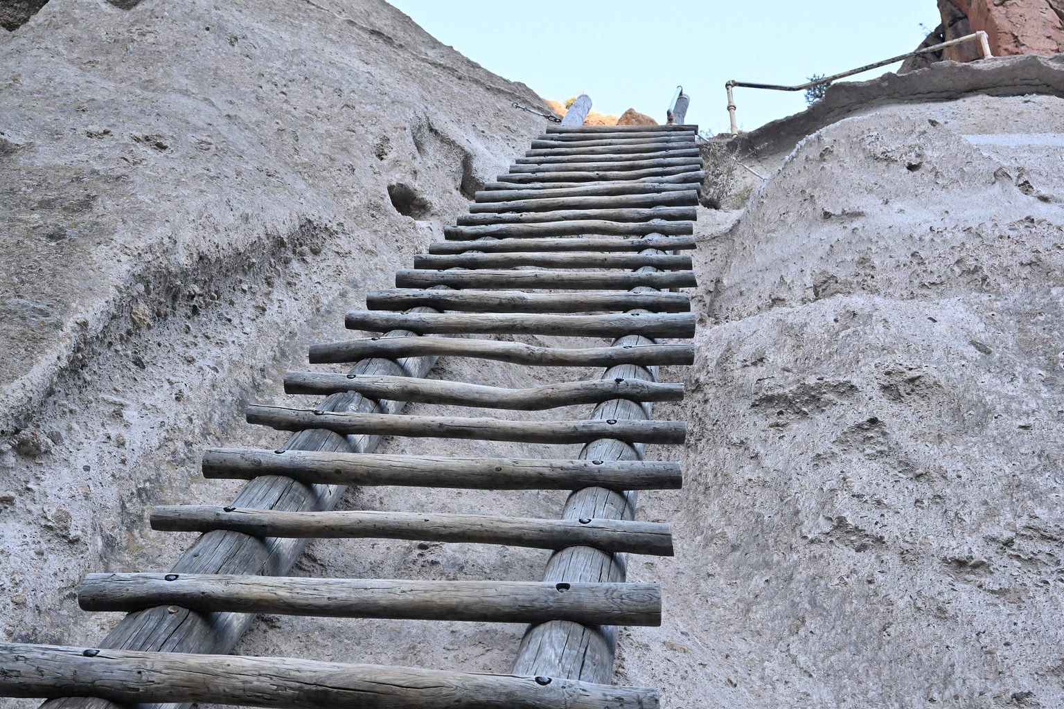 Eine Holzleiter führt steil an einer hellen Felswand hinauf zu einer Öffnung im Fels