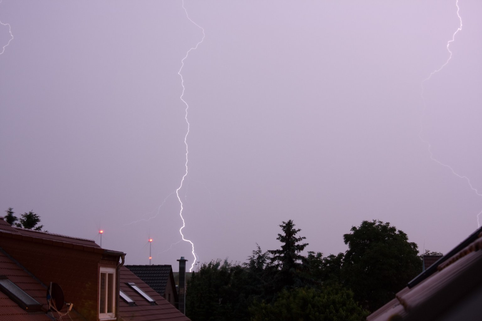 Ein Blitz am violetten Abendhimmel über Dächern und Bäumen