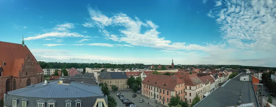 Blick über die Dächer von Bernau bei Berlin mit der Marienkirche links, Straßen mit Altbauten und Wald am Horizont unter blauem Himmel