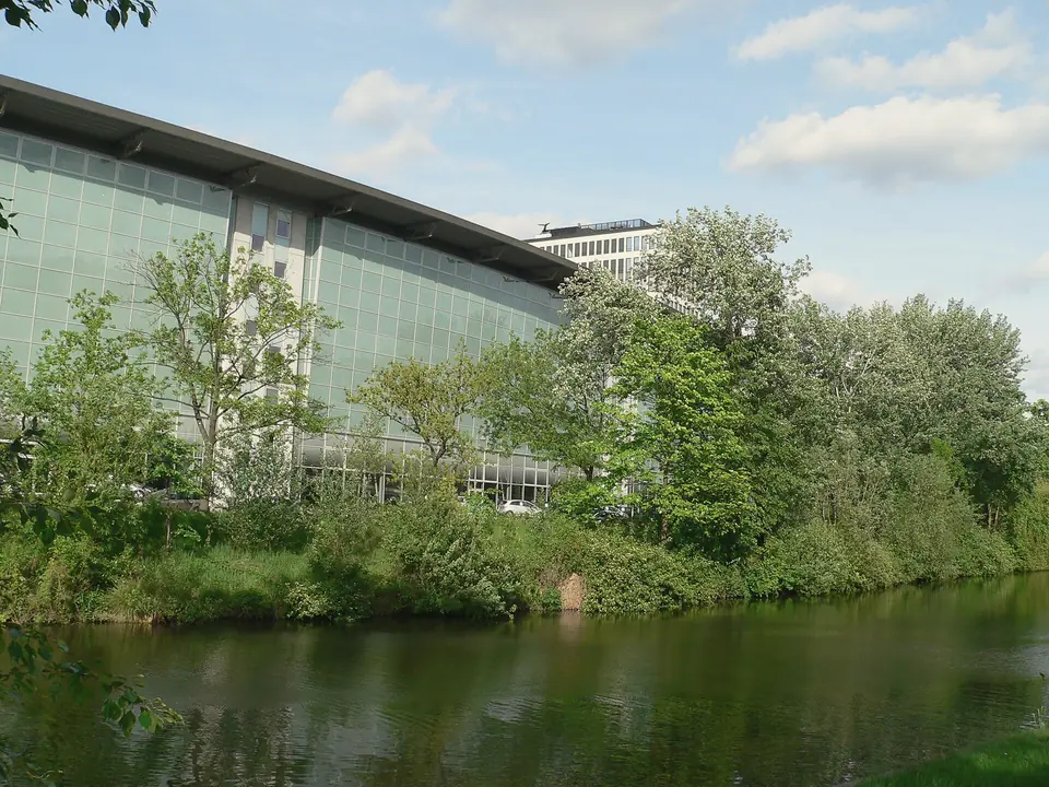 Der Landwehrkanal am Salzufer mit begrüntem Ufer, dahinter ein Bürogebäude mit Glasfassade