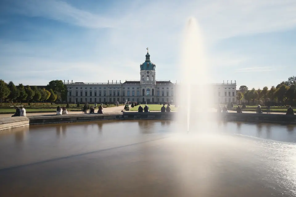 Schloss Charlottenburg vom Schlossgarten aus, im Vordergrund ein Wasserbecken mit Fontäne unter blauem Himmel