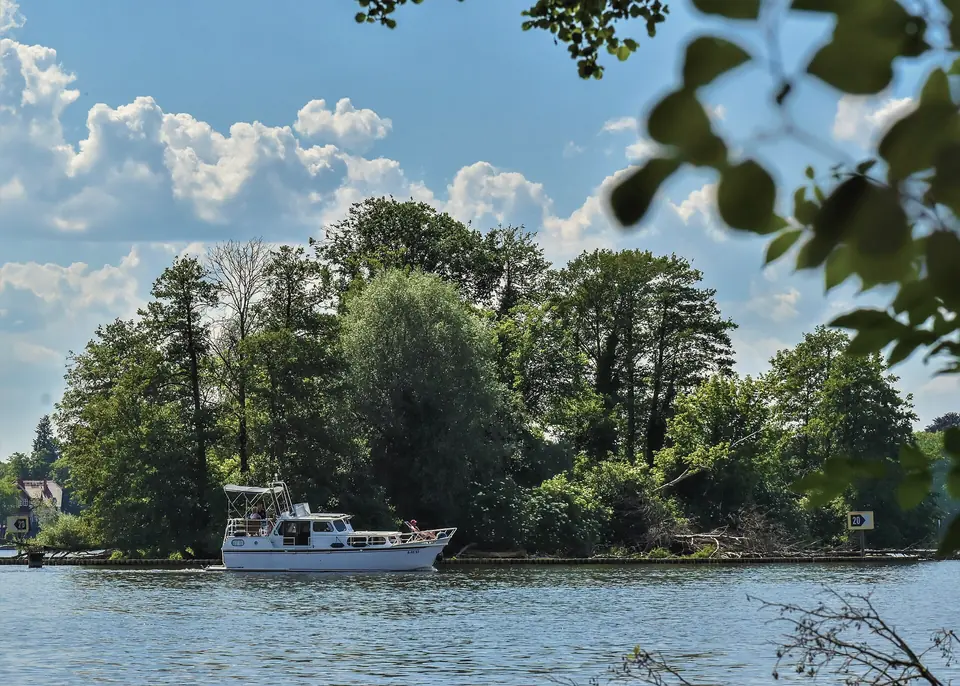Bewaldete Insel Zeuthener Wall im Zeuthener See, davor ein Motorboot auf dem Wasser, blauer Himmel mit Wolken
