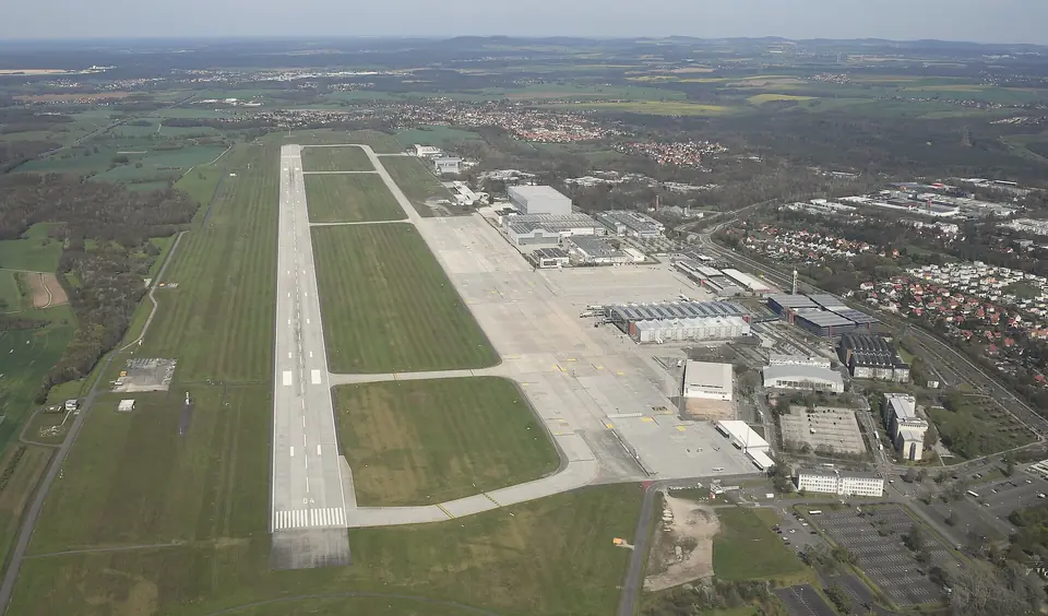 Luftbild des Flughafens Dresden mit Start- und Landebahn, rechts daneben die Wohngebiete von Klotzsche, dahinter Wald und Felder