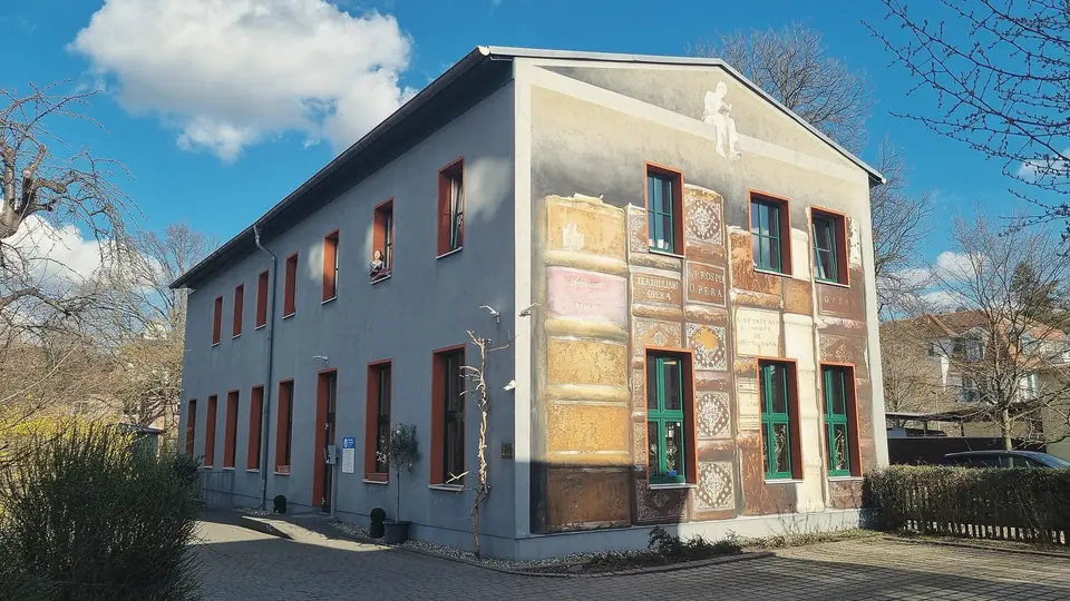 Zweigeschossiges Gebäude der Bibliothek Laubegast, die Giebelseite mit aufgemalten Buchrücken, blauer Himmel mit einer Wolke