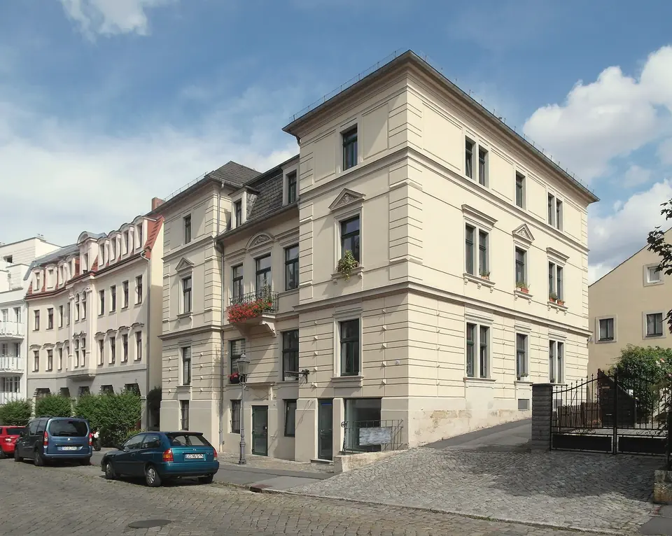 Saniertes viergeschossiges Wohnhaus an der Dohnaer Straße in Strehlen an einer gepflasterten Straße mit parkenden Autos, blauer Himmel mit Wolken