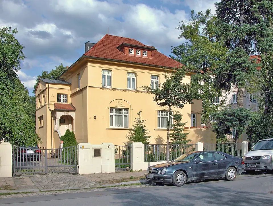 Eine gelbe Villa mit rotem Ziegeldach in der Heubnerstraße hinter einem Zaun, davor ein parkendes Auto
