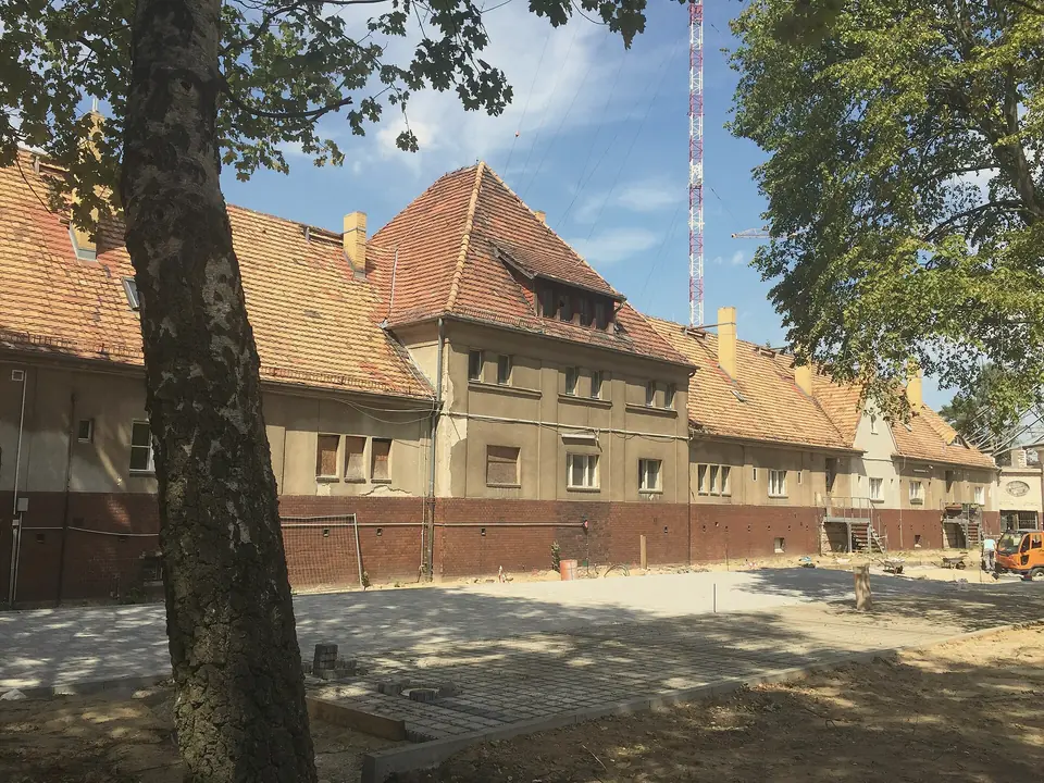 Lange Gebäude mit roten Ziegeldächern auf dem Funkerberg, davor ein neu gepflasterter Platz, im Hintergrund ein Sendemast