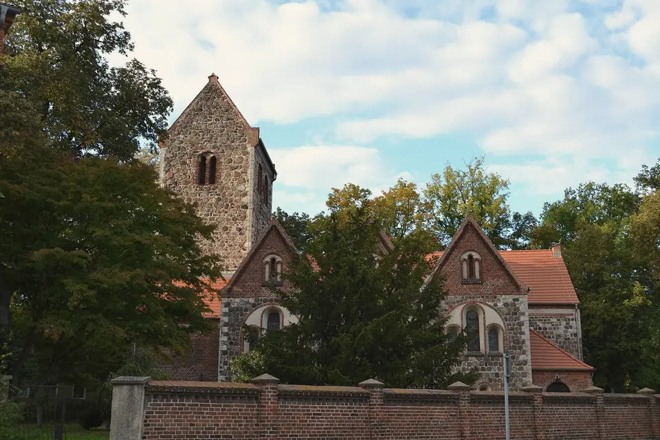 Die Dorfkirche Neuenhagen aus Feldsteinen mit Backsteingiebeln und Turm, davor eine Backsteinmauer und Bäume