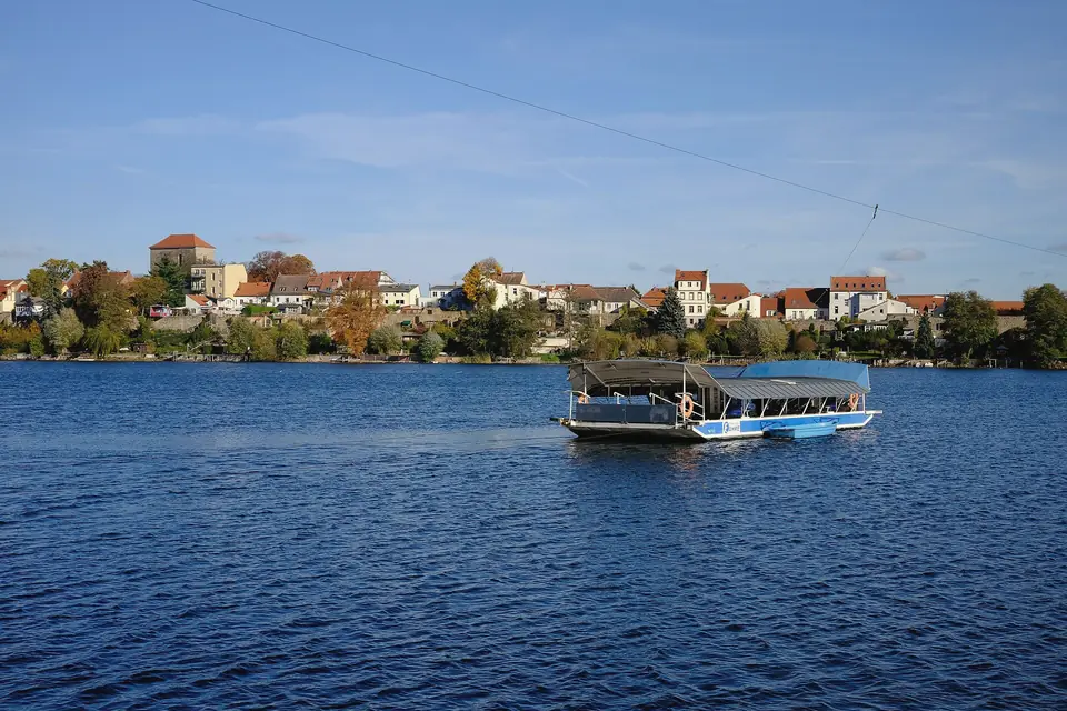 Die Strausseefähre auf dem blauen Straussee, dahinter die Altstadt von Strausberg mit roten Dächern und herbstlichen Bäumen