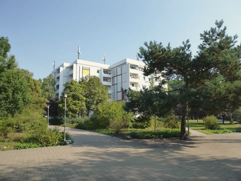 Ein Platz mit Bäumen und Beeten in Hennigsdorf, dahinter ein weißes Wohnhochhaus