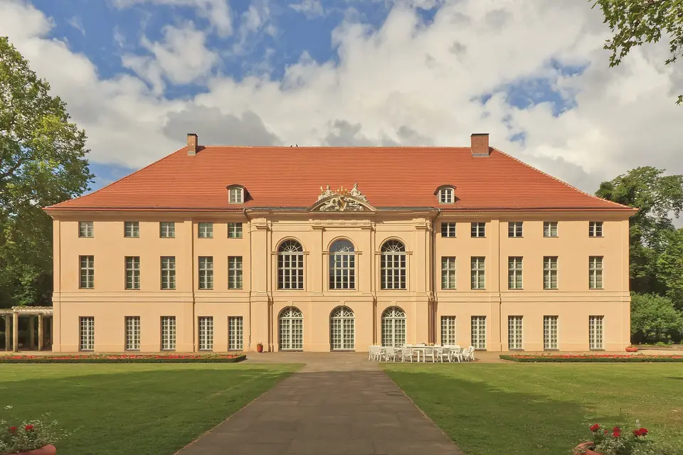 Gartenseite von Schloss Schönhausen mit hellem Putz und rotem Dach, davor Rasen und ein gerader Weg
