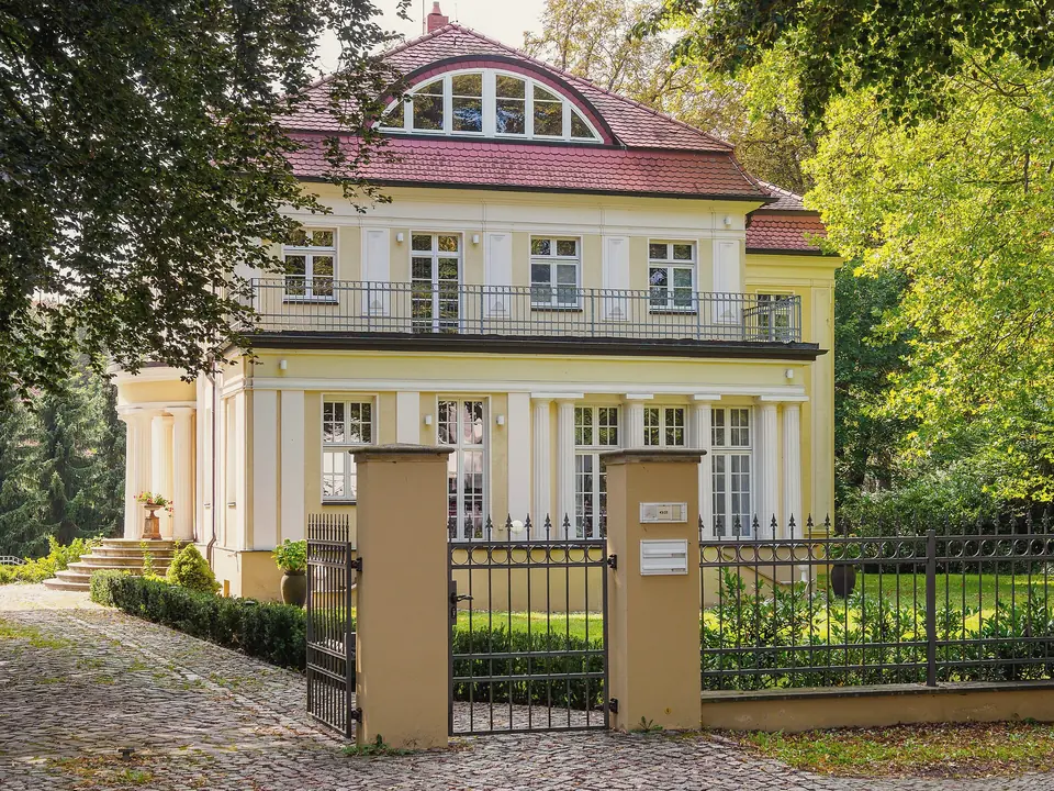 Eine helle Villa mit Balkon und rundem Giebelfenster hinter einem Tor mit Pfeilern in der Karl-Marx-Straße in Babelsberg
