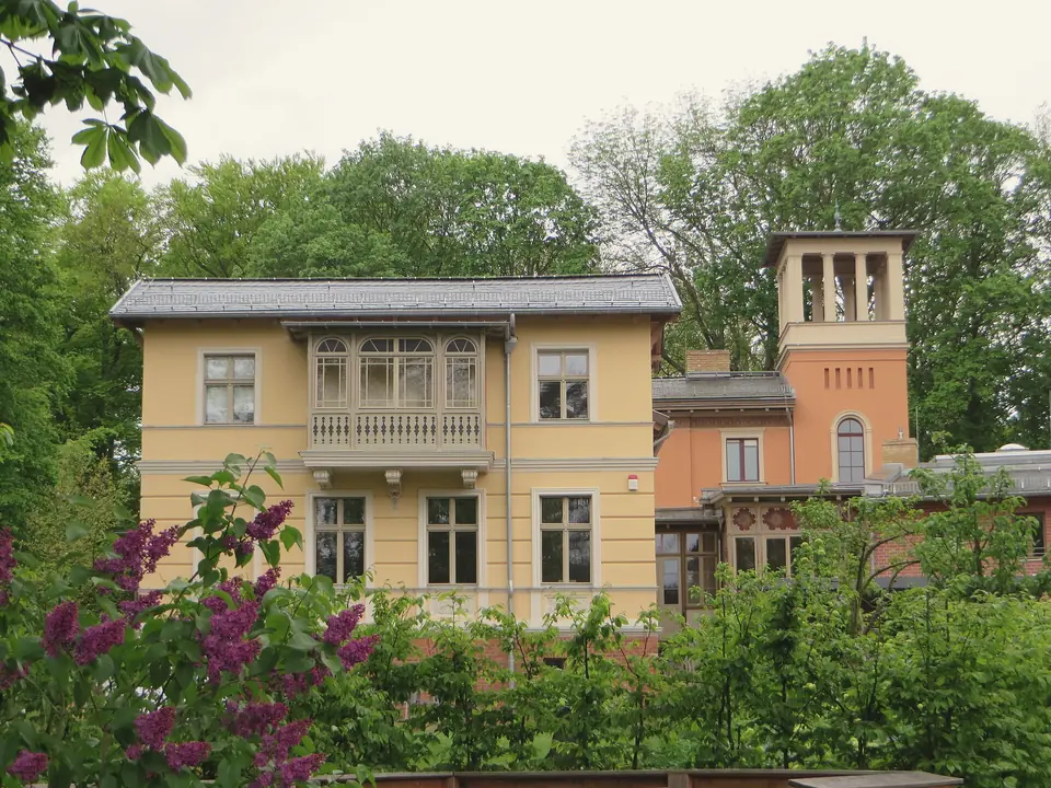 Eine gelbe Villa im italienischen Stil mit Turm und Loggia in der Ribbeckstraße in Bornstedt, davor blühende Sträucher