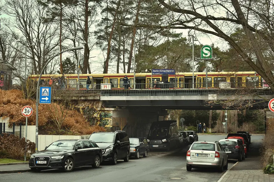 S-Bahn auf der Brücke am S-Bahnhof Schlachtensee, darunter eine Straße mit parkenden Autos und Kiefern