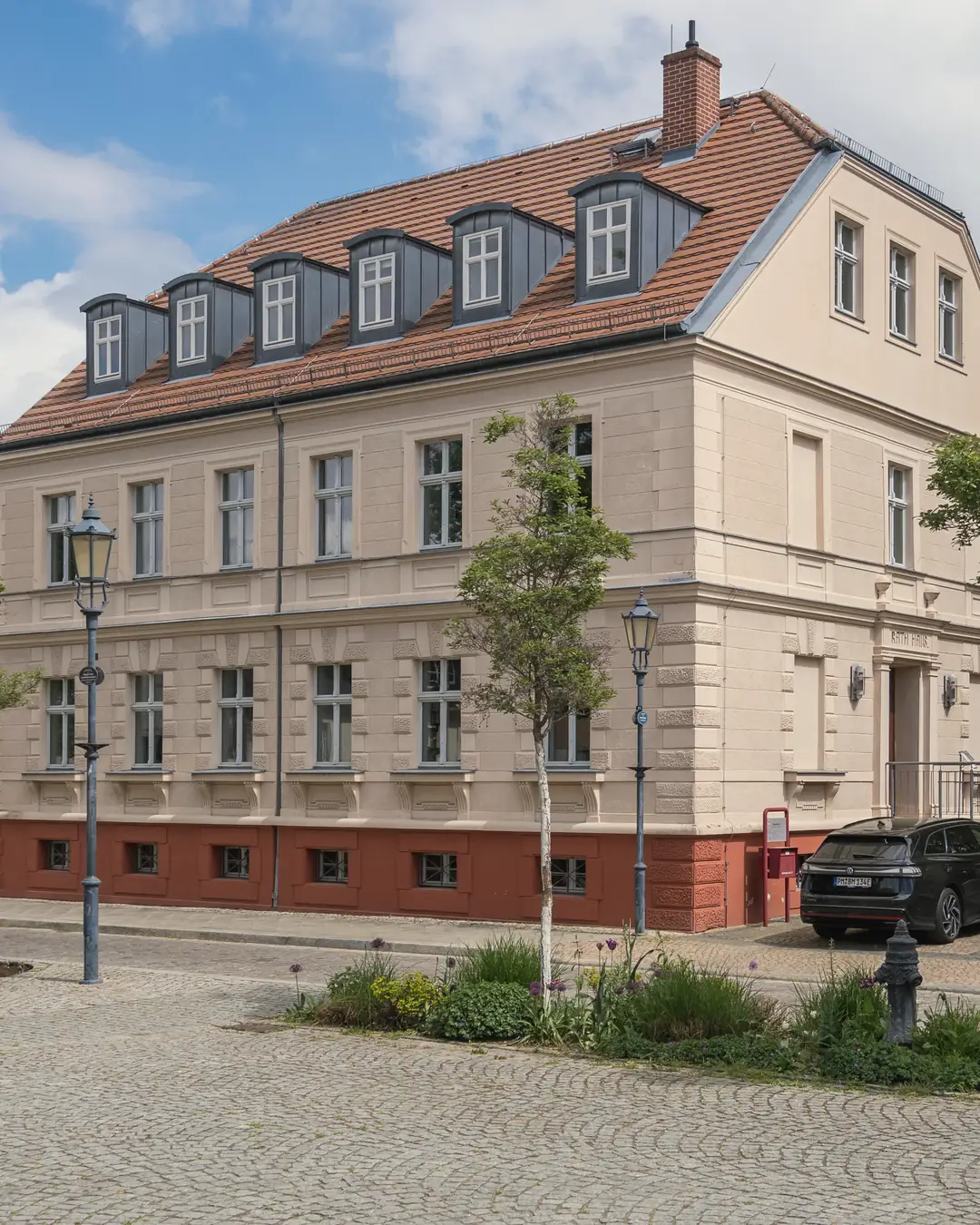 Das Alte Rathaus in Teltow an einem sonnigen Tag, davor ein gepflasterter Platz und junge Bäume