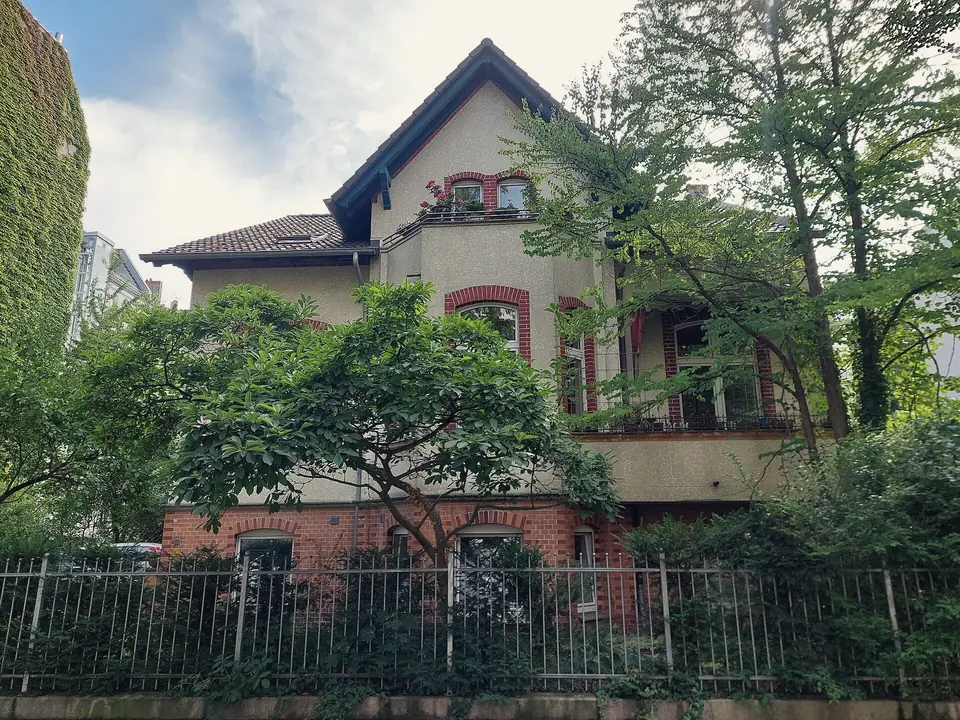 Das Landhaus Pählchen in der Görresstraße mit Backsteinsockel und Balkon, hinter Bäumen und einem Eisenzaun