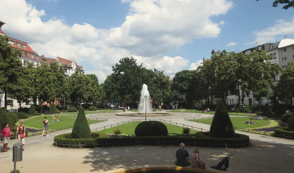 Der Viktoria-Luise-Platz im Sommer mit Springbrunnen, Rasenflächen und geschnittenen Hecken, ringsum Altbauten und Bäume