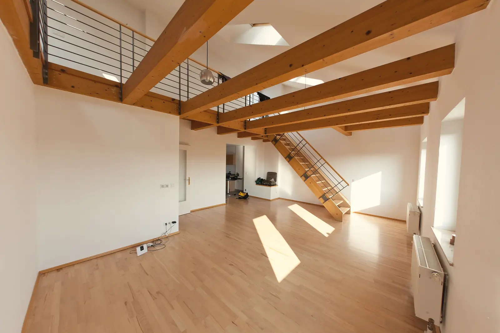 Heller, leerer Altbauraum mit Holzbalken an der Decke, Dielenboden und einer Treppe