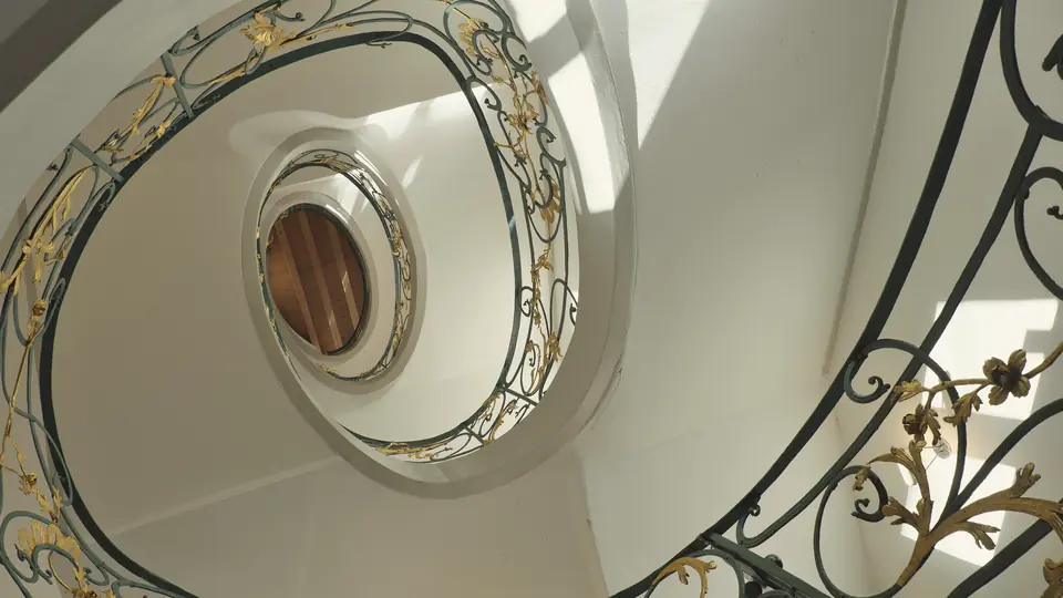 Blick nach oben in ein gewendeltes Altbau-Treppenhaus mit verziertem Geländer in Berlin-Mitte