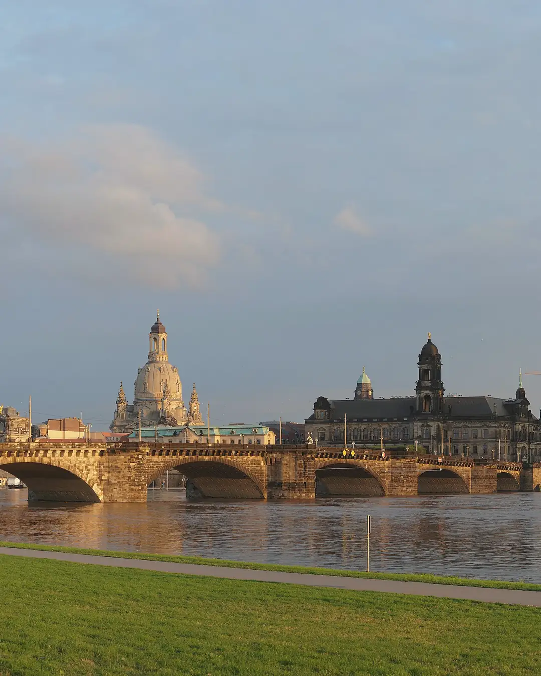 Canaletto-Blick in Dresden: die Augustusbrücke über die Elbe, dahinter Frauenkirche und Hofkirche im warmen Licht, vorn die Elbwiesen